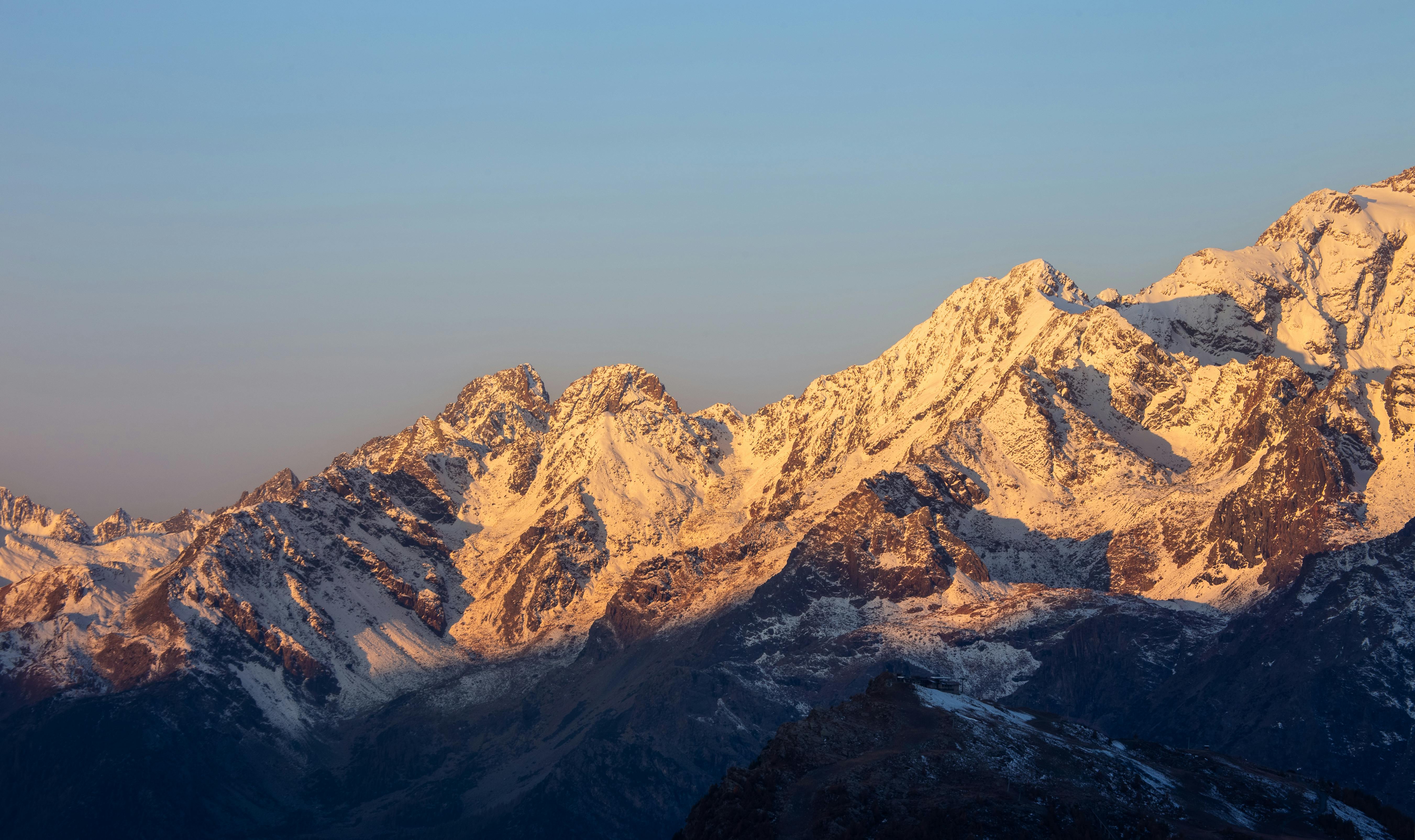美景图片自然风景_身穿橙色夹克的徒步旅行者俯瞰阿尔卑斯山日落